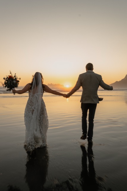 Couple running together toward the ocean at golden hour